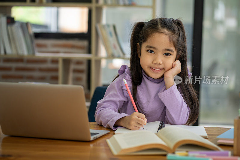 Young Asian girl doing homework online using laptop computer to improve her learning skills.